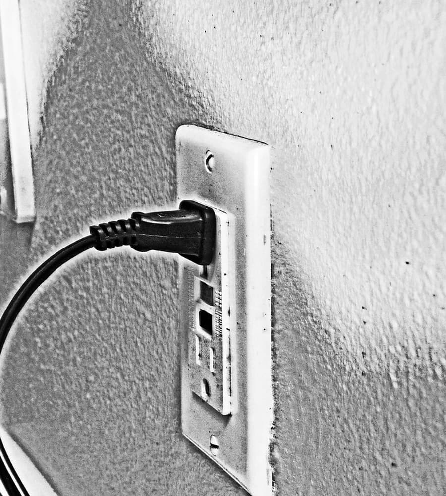 Nahaufnahme einer Wandsteckdose mit eingestecktem Stecker, Schwarz-Weiß-Aufnahme